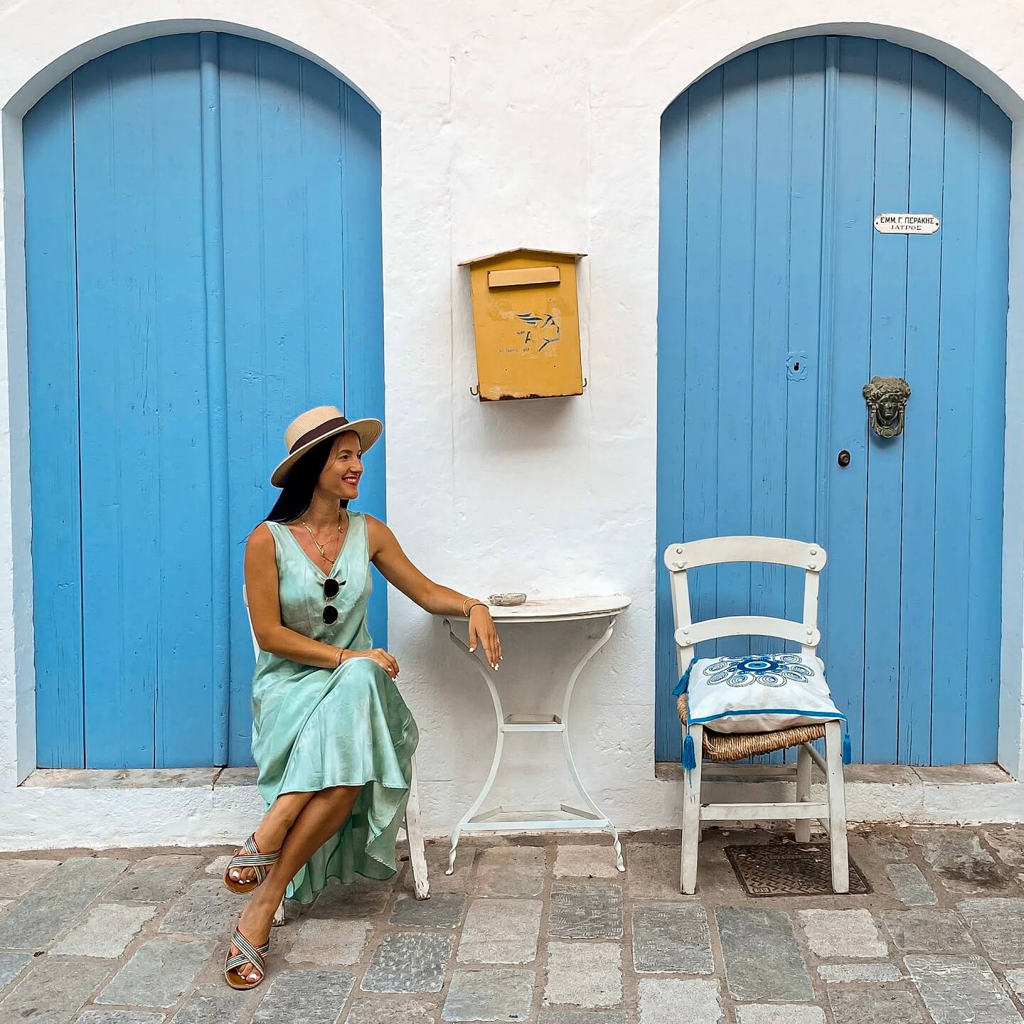Stella sitting in front of the blue doors in Kritsa, Crete