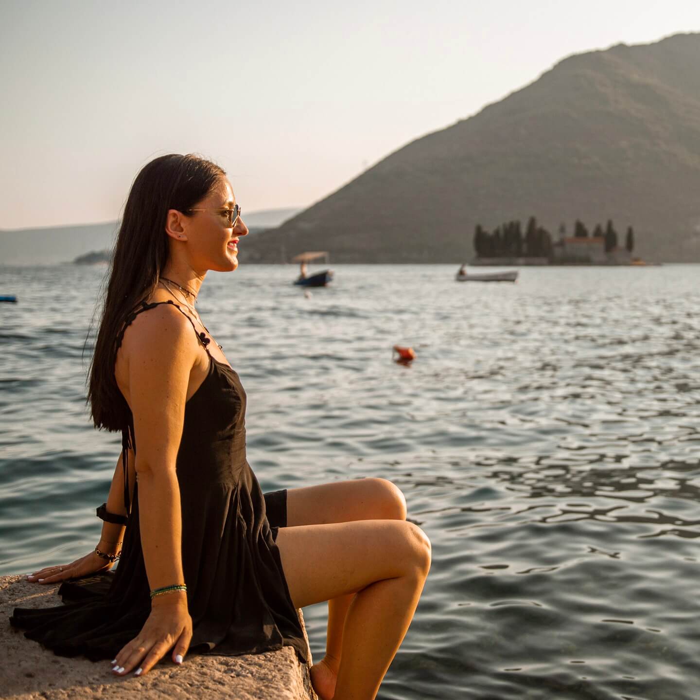 Stella sitting by the sea with Our Lady of the Rocks in the background